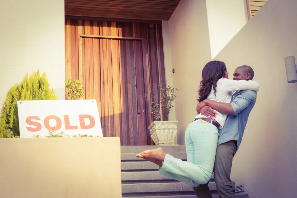 Couple embracing happily in front of home with "SOLD" sign